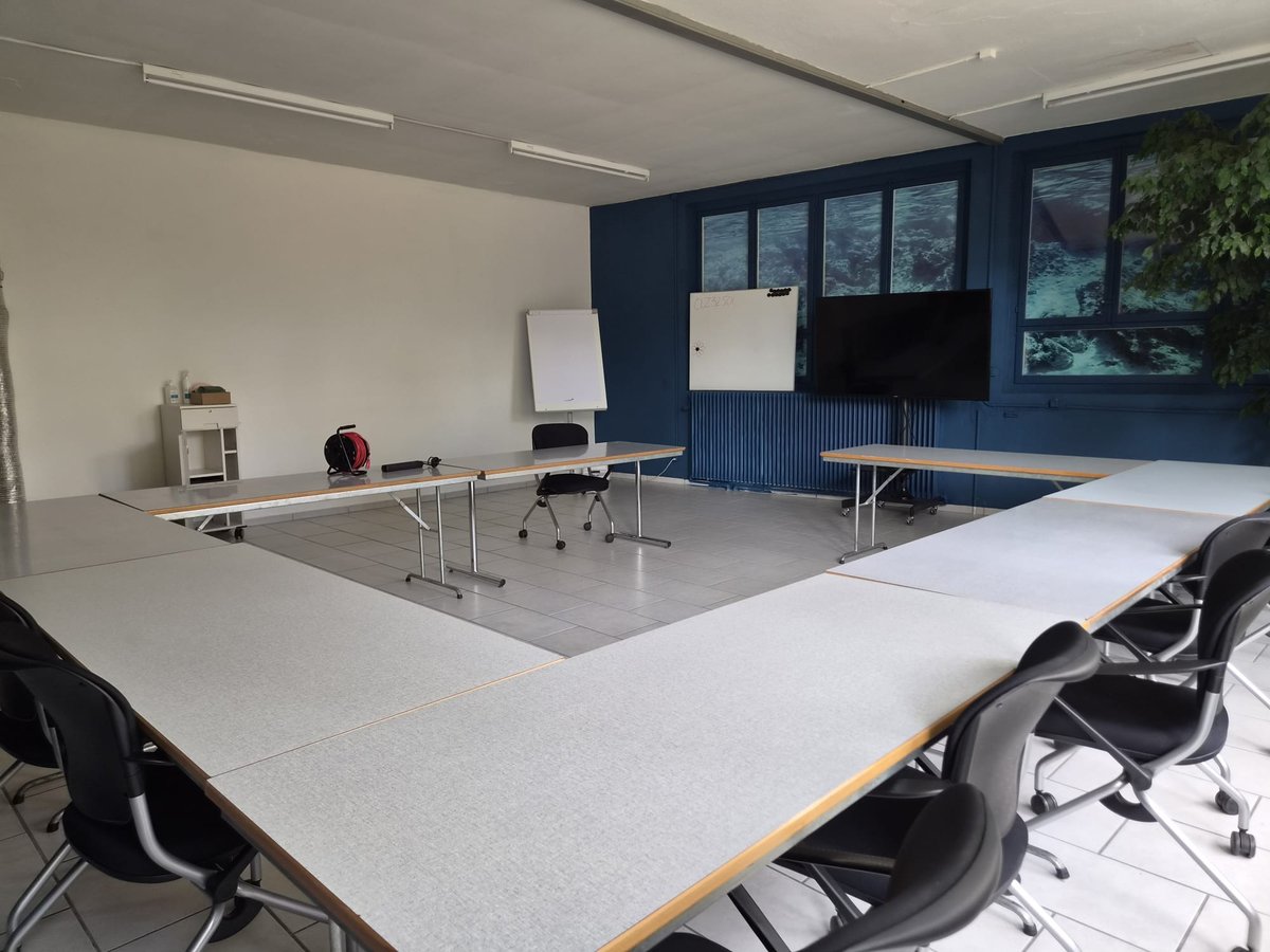 Kursraum mit Tischen, grossem Bildschirm und Whiteboard.
